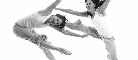 Two dancers pose while jumping into the air.